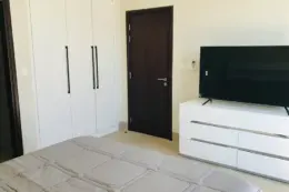 A simple, modern bedroom with a TV on a white dresser, a wardrobe, and a door.